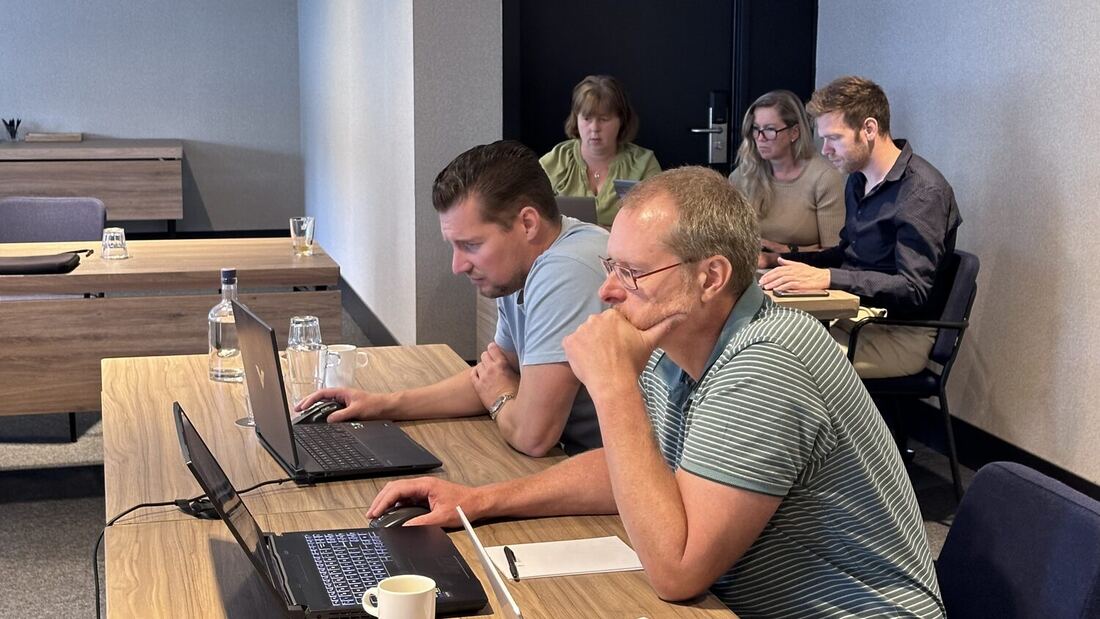 Two delegates work at a laptop with others at the table behind them.