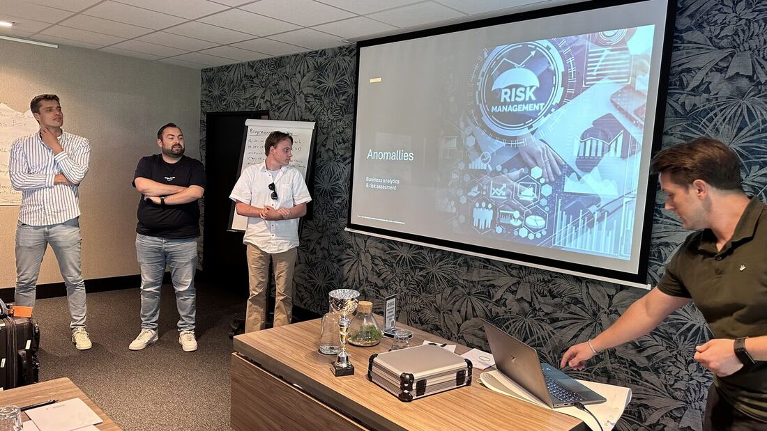 Three students stand at the front of the room as their title slide plays on the screen.