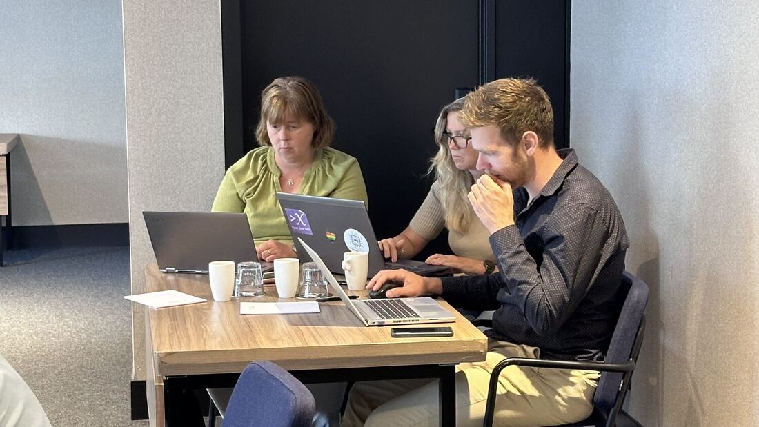 Three delegates work together at a laptop in a corner of the room.