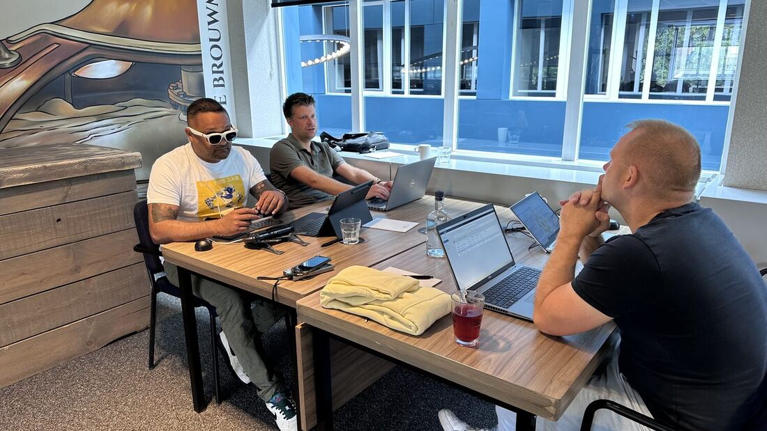 Three delegates at a table with laptops under the mural.