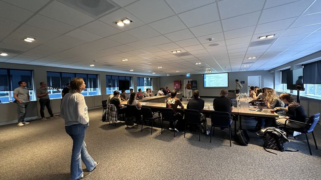 The room from the side, delegates at the table with the screen lit at the far wall.