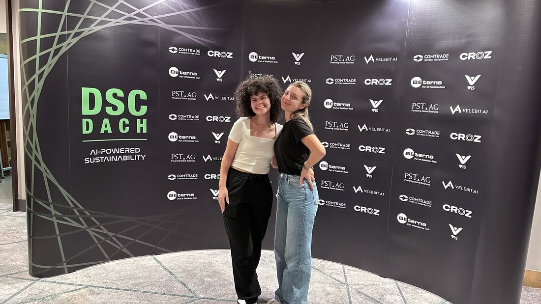 Two attendees photographed in front of the DSC DACH sponsor wall, the theme AI-powered sustainability printed at the left.