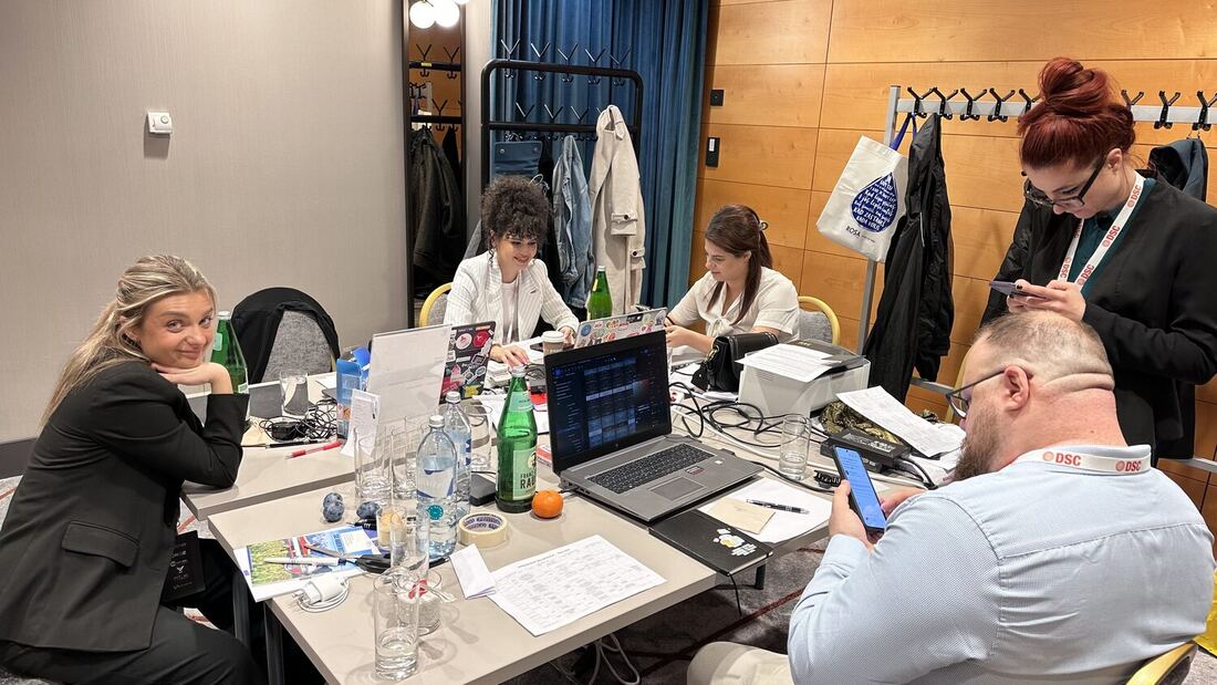 Members of the crew work from laptops around a table off the main hall, badges and lanyards on the table.