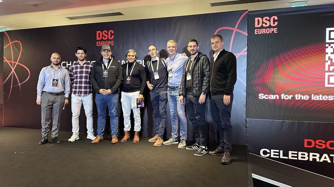 Eight people stand together in front of the DSC Europe wall