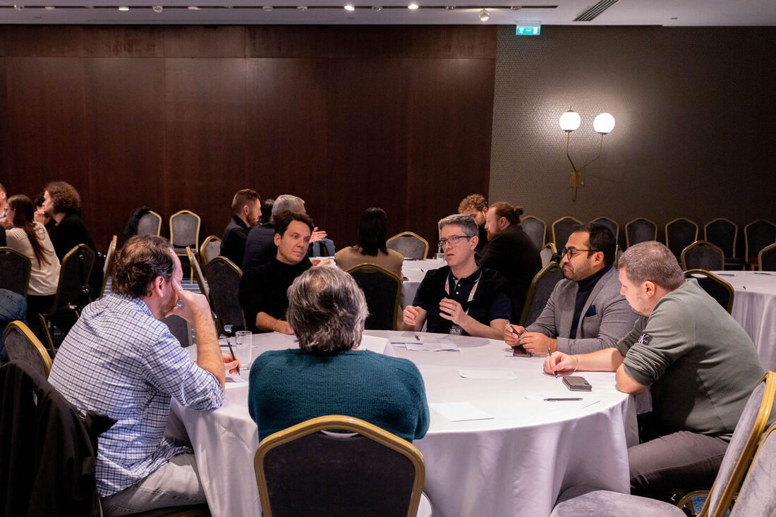 Round tables of delegates working, a screen lit behind them