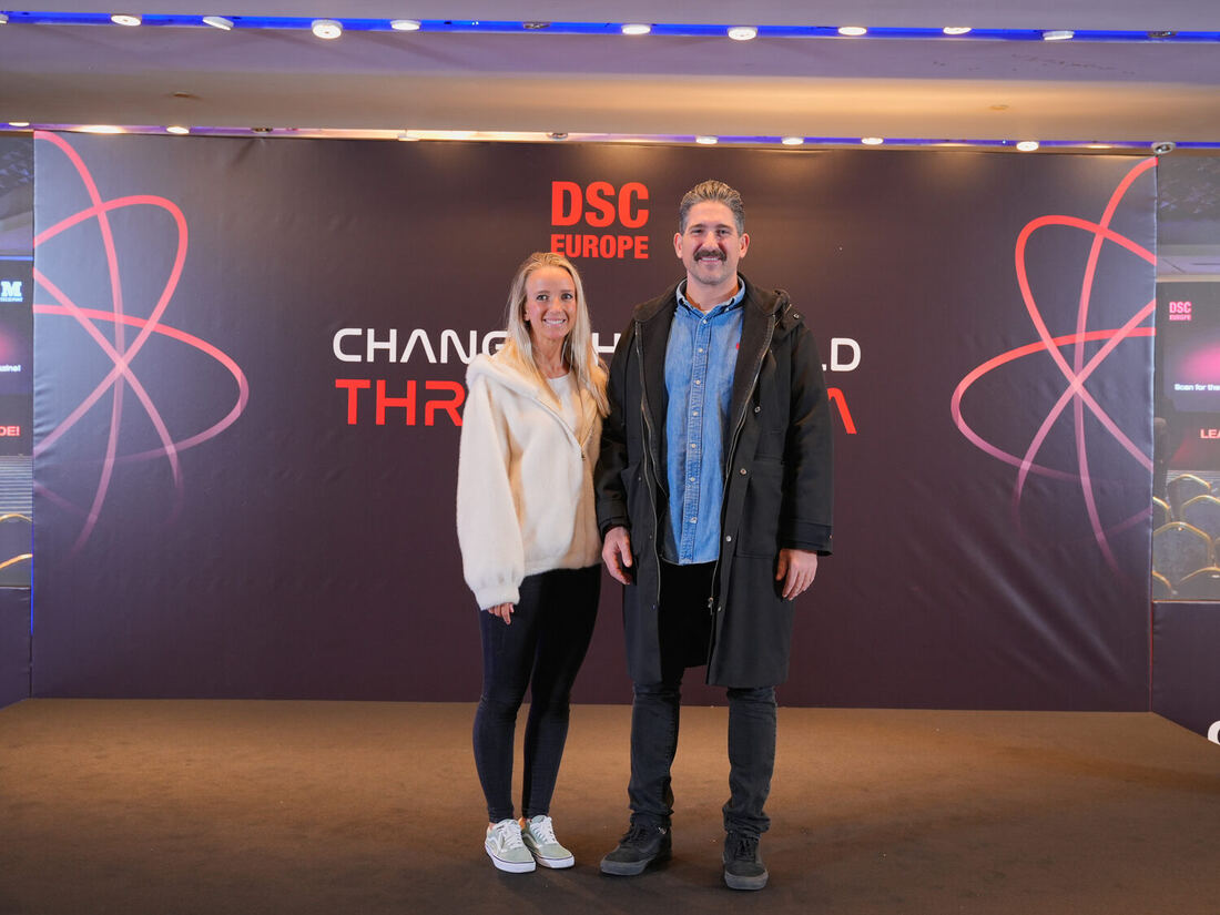 Two people stand in front of the DSC Europe photo wall