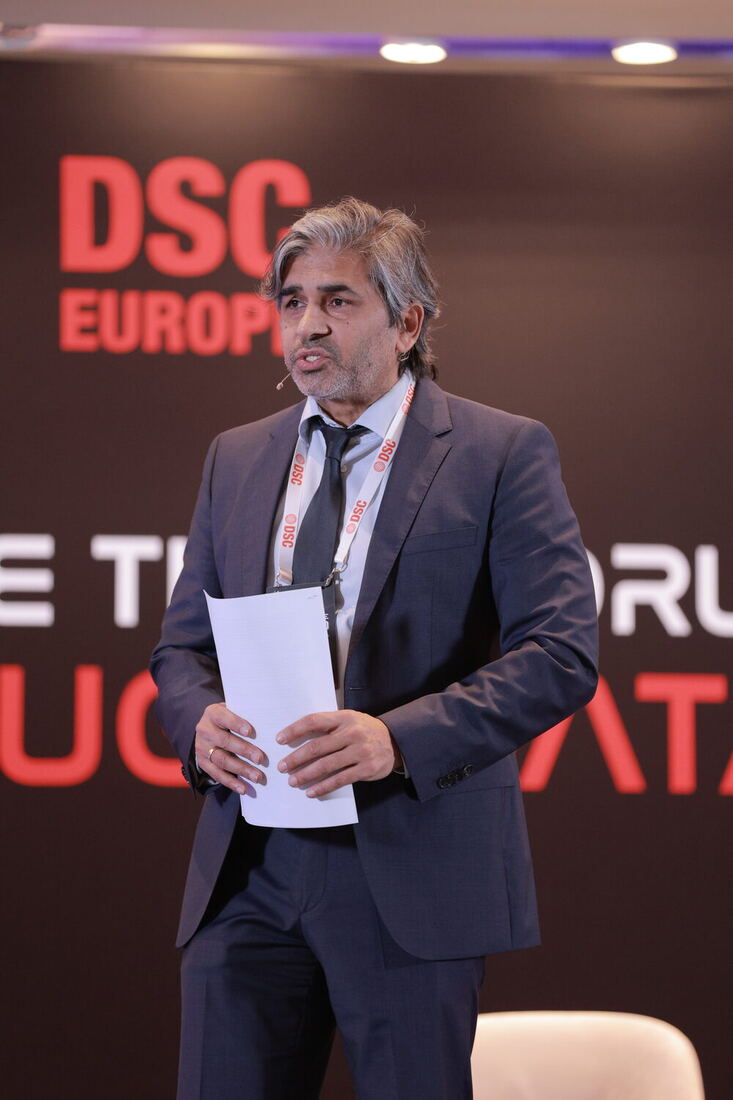 The host on stage with notes in hand in front of the DSC Europe backdrop