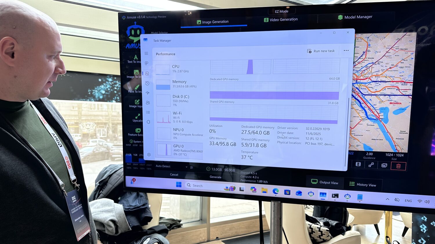 AMD demo screen with Windows task manager open over the image generator, showing GPU memory and temperature, watched by a delegate with a speaker badge.