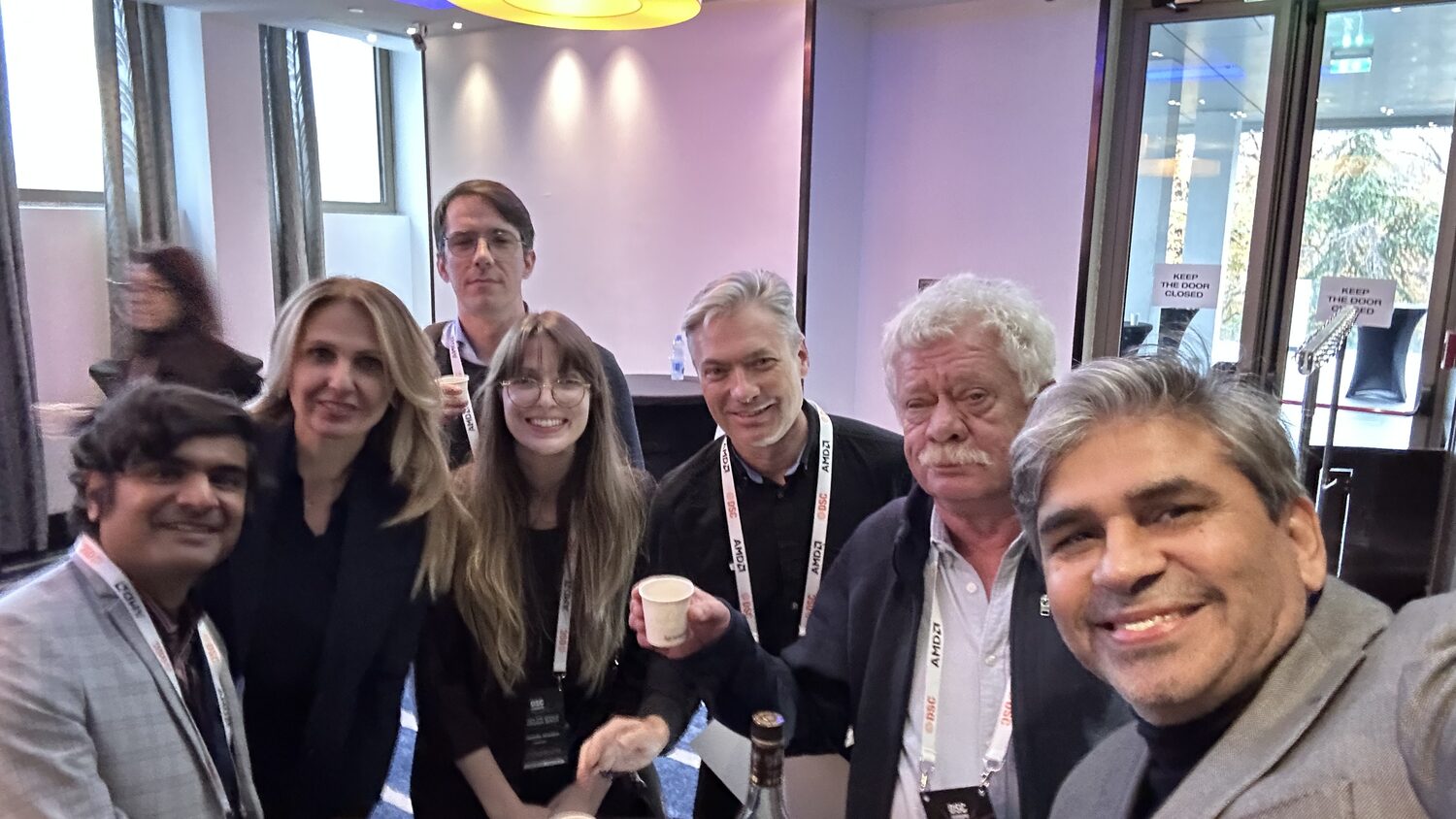 Group of seven with DSC and AMD lanyards standing together in a break area with coffee cups.