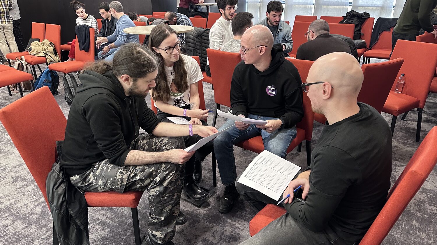 Four participants in a circle of red chairs, reading a printed AI Strategy Canvas handout