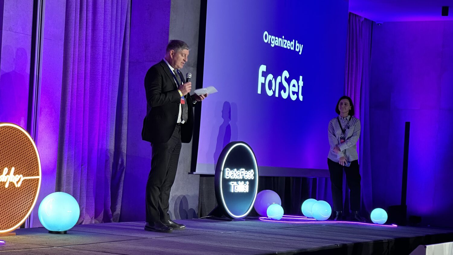 Two hosts on the DataFest Tbilisi stage, the screen behind reading Organized by ForSet