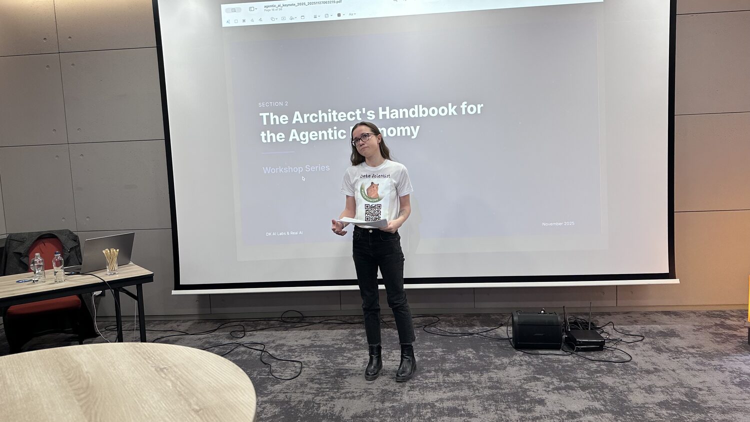 A participant presenting to the workshop room, the screen behind reading The Architect's Handbook for the Agentic Economy, DK AI Labs and Real AI