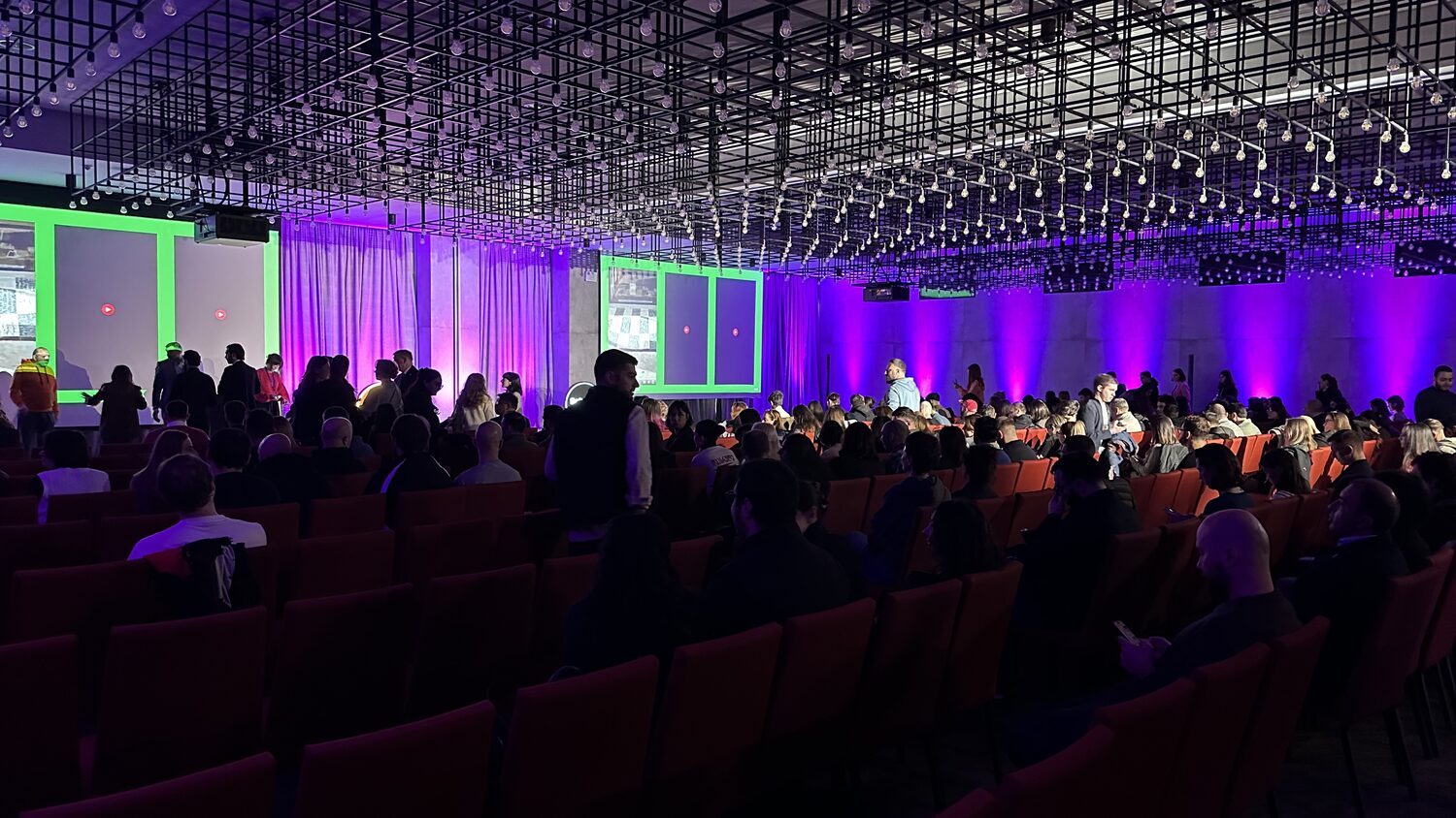 The main hall filling before a session, purple stage lighting over rows of red seats
