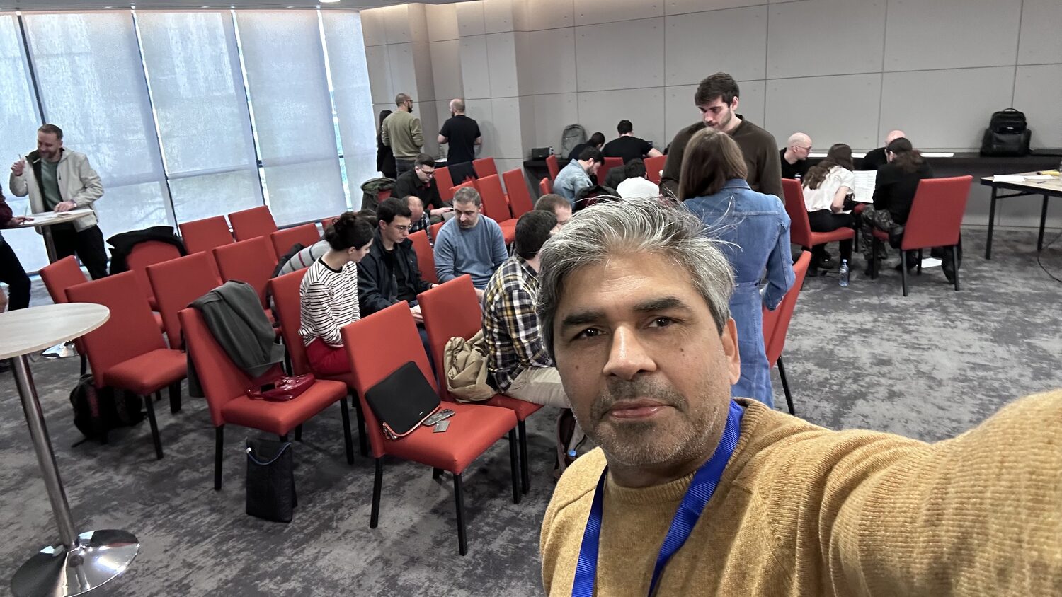 The workshop room mid session, participants at tables and in rows of red chairs, seen from the back
