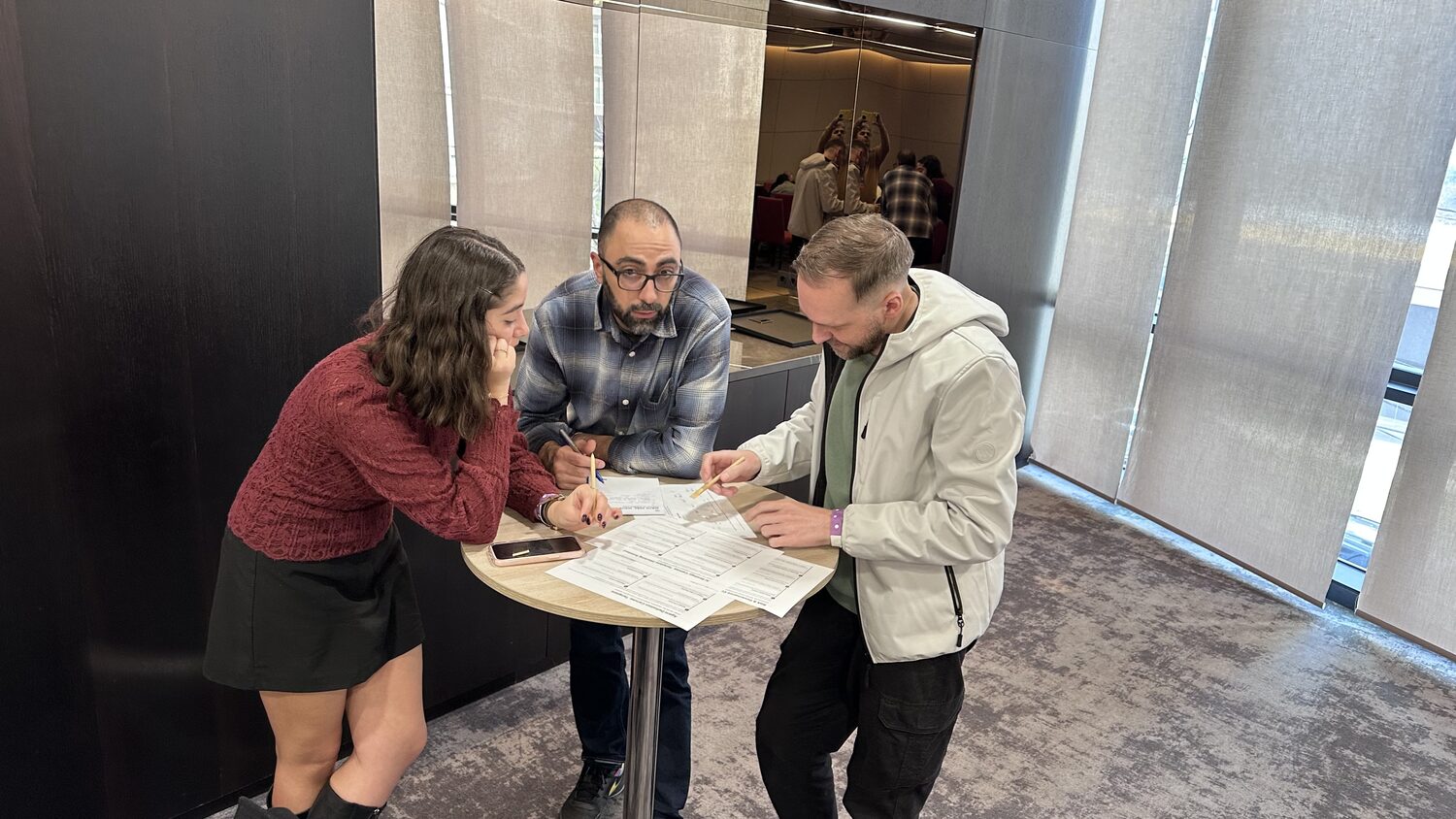 Three participants standing at a high round table, filling in the printed canvas with pencils