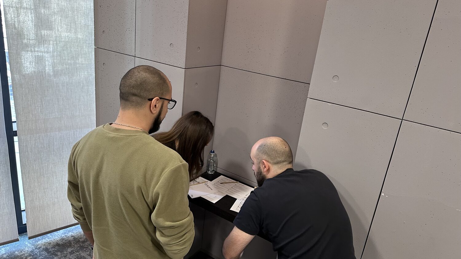 Three participants leaning over a wall ledge, working on the printed handout