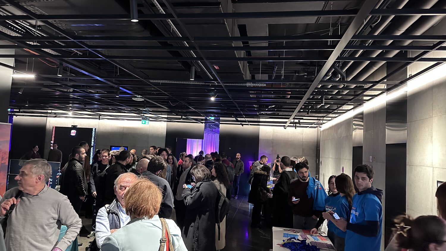 Conference foyer between sessions, volunteers in blue DataFest 2025 shirts at a table by the lifts