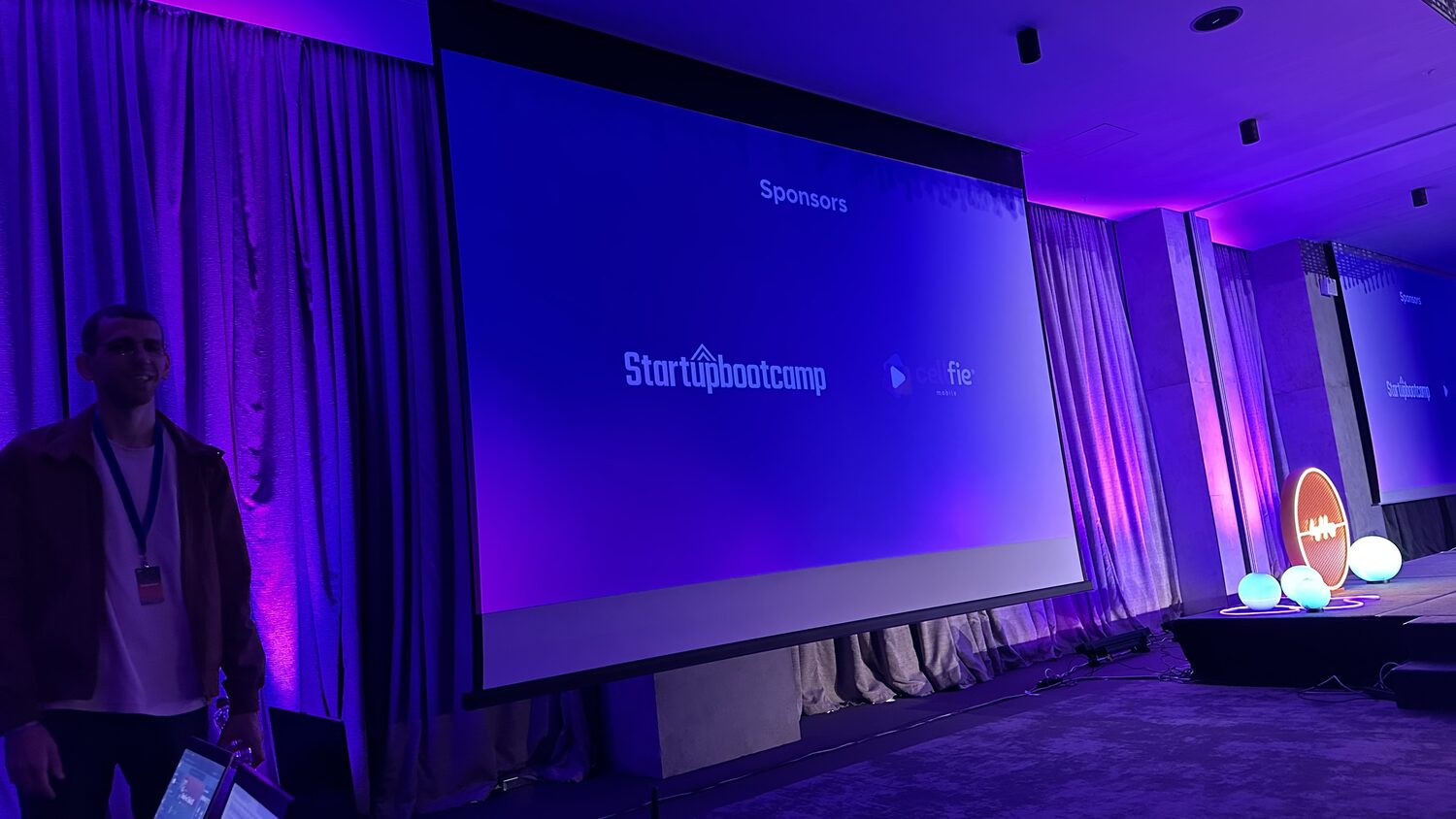 Sponsors slide on the main screen reading Startupbootcamp and Cellfie Mobile, a crew member standing beside it