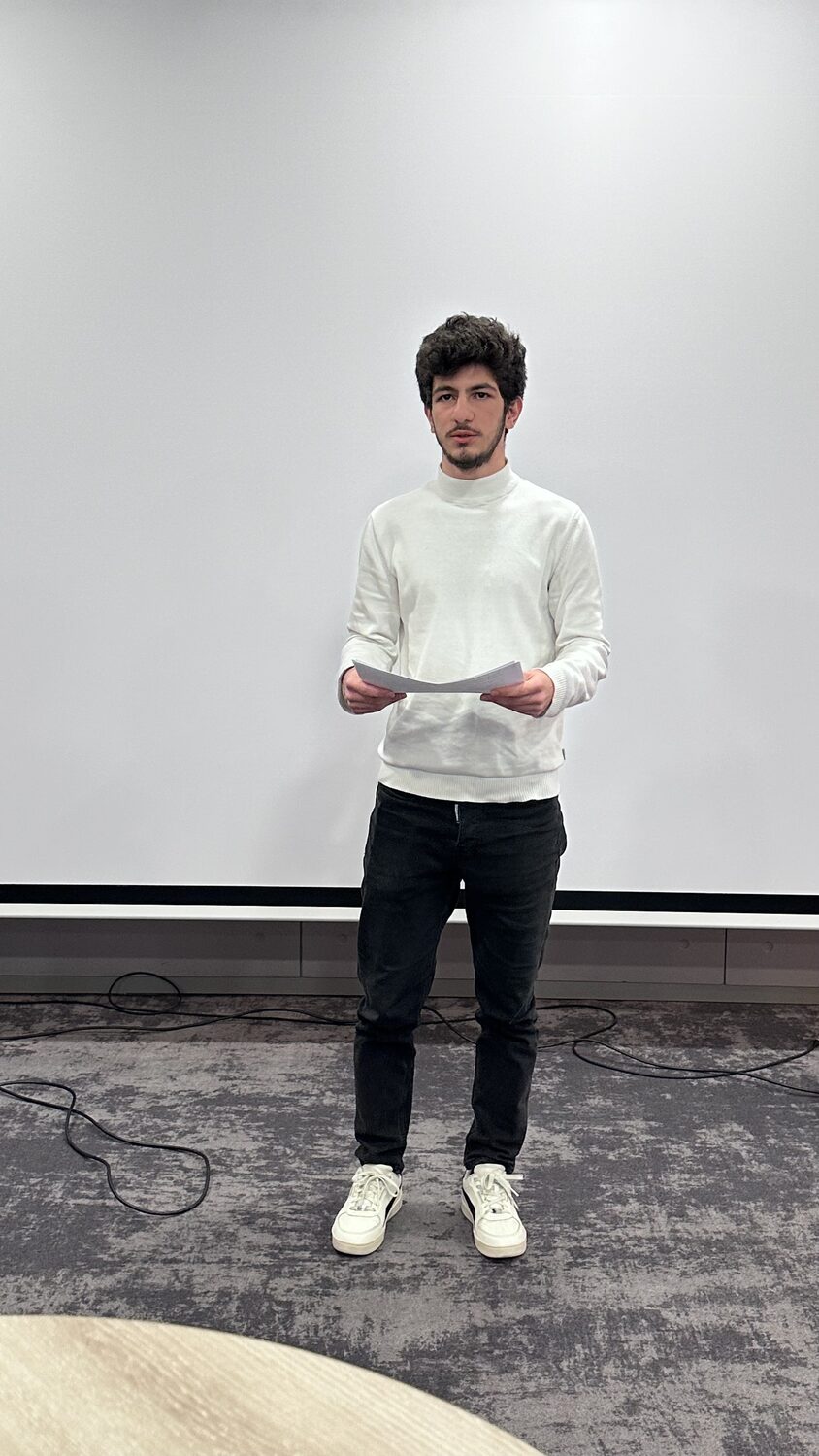 A participant standing at the front of the workshop room with printed notes in his hands