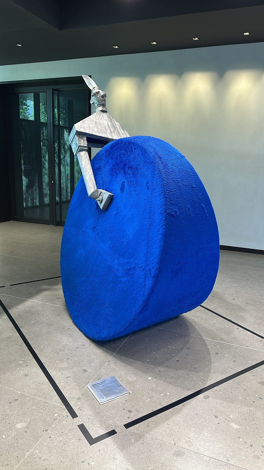 Mrdjan Bajic's sculpture Hidrocentrala in an office lobby, a bronze figure leaning against a large disc covered in blue fur, its plaque on the floor.