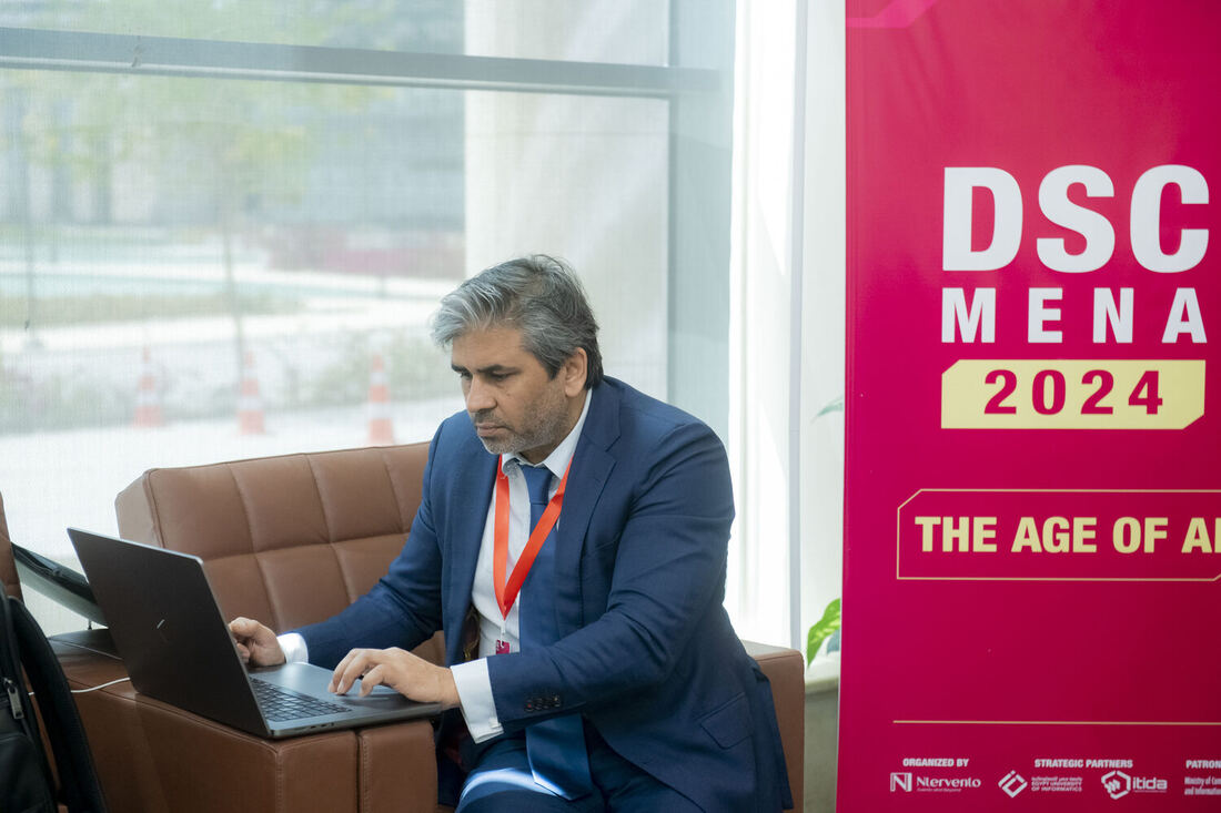 Tarry Singh working on a laptop in the venue foyer beside a DSC MENA 2024 banner.