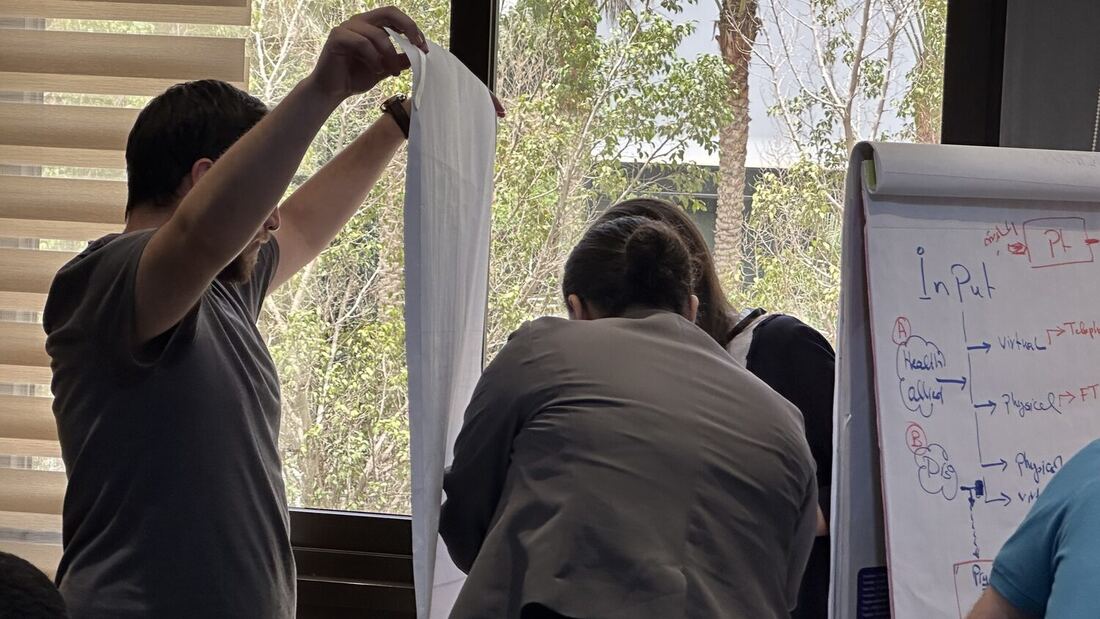 Participant lifting a fresh sheet onto the flip chart while the group works around him