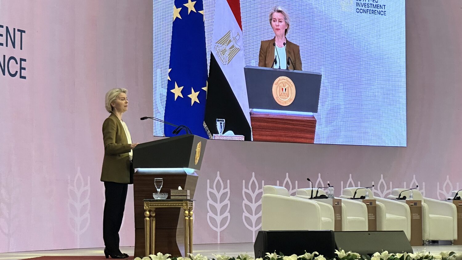 Ursula von der Leyen addresses the conference from the podium, her image relayed on the screen behind her between the EU and Egyptian flags.