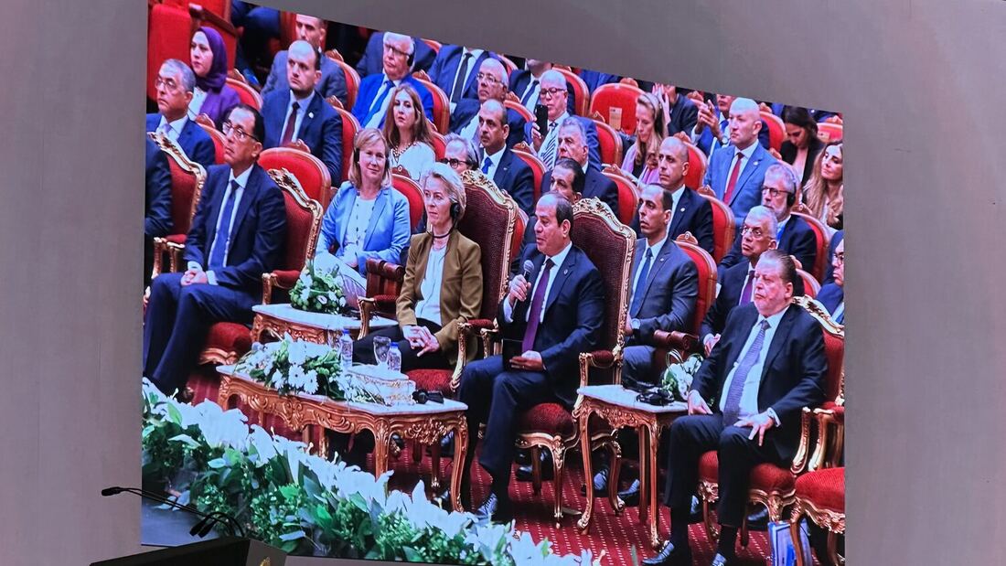 The relay screen shows El-Sisi speaking with a microphone from his seat in the front row, von der Leyen beside him.