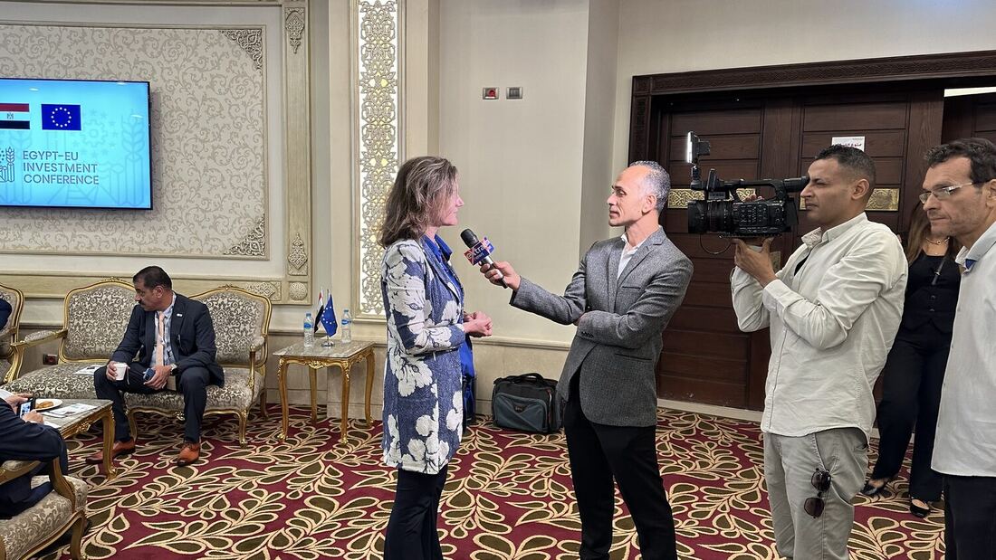 An Egyptian television crew films an interview in the delegates' lounge, the conference screen mounted on the wall behind.