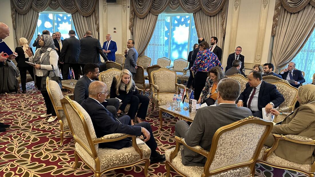 The delegates' lounge during a break, groups seated in gilt armchairs and standing across the room.