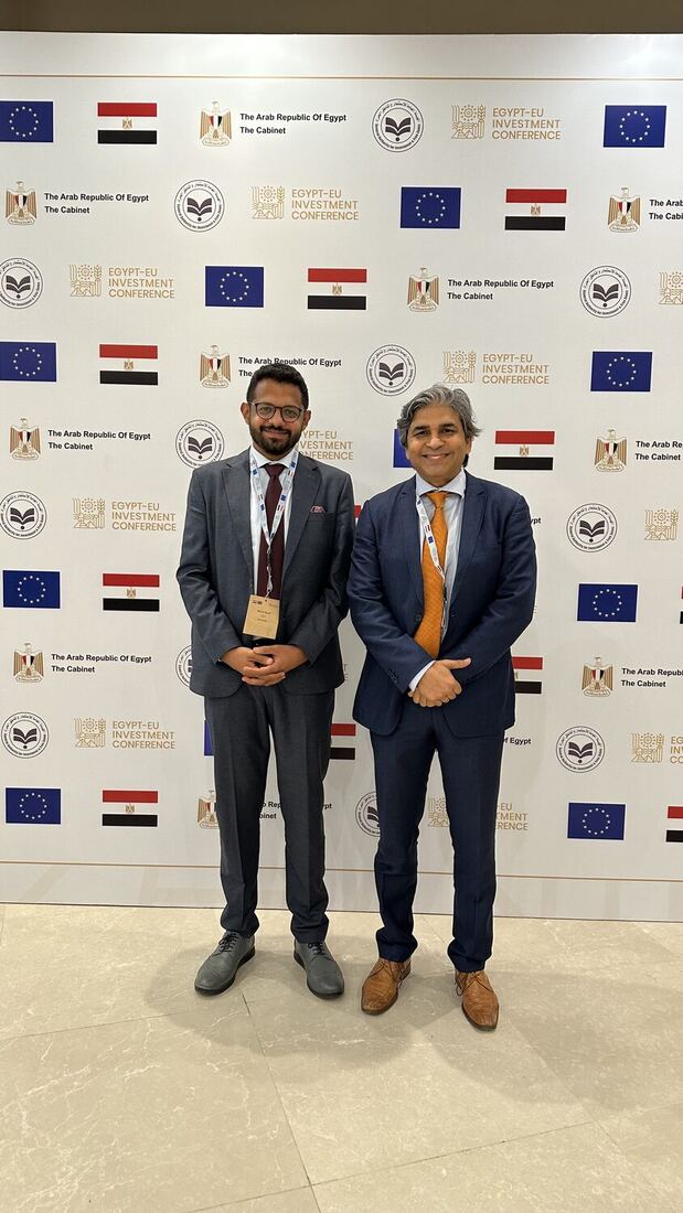 Two delegates standing at the step-and-repeat wall of the Egypt-EU Investment Conference.