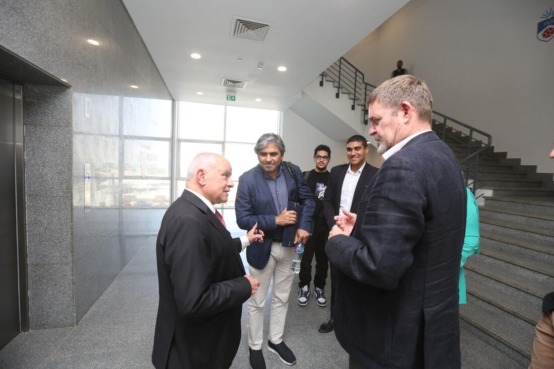 Conversation in the lift lobby between Tarry Singh and two hosts, students waiting by the staircase behind them.