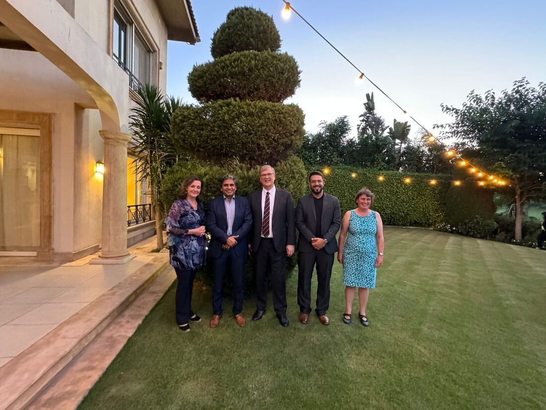 Evening group photograph of five people on a lawn outside a residence, string lights overhead.