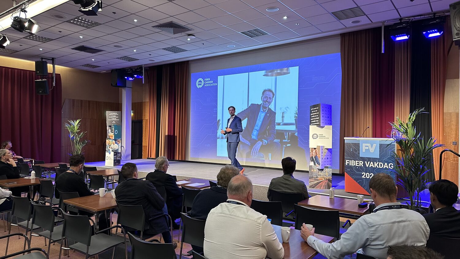 A morning session under way at the Fiber Vakdag, delegates at tables facing a speaker on stage, with the FIBER VAKDAG 2024 lectern at the right of frame.