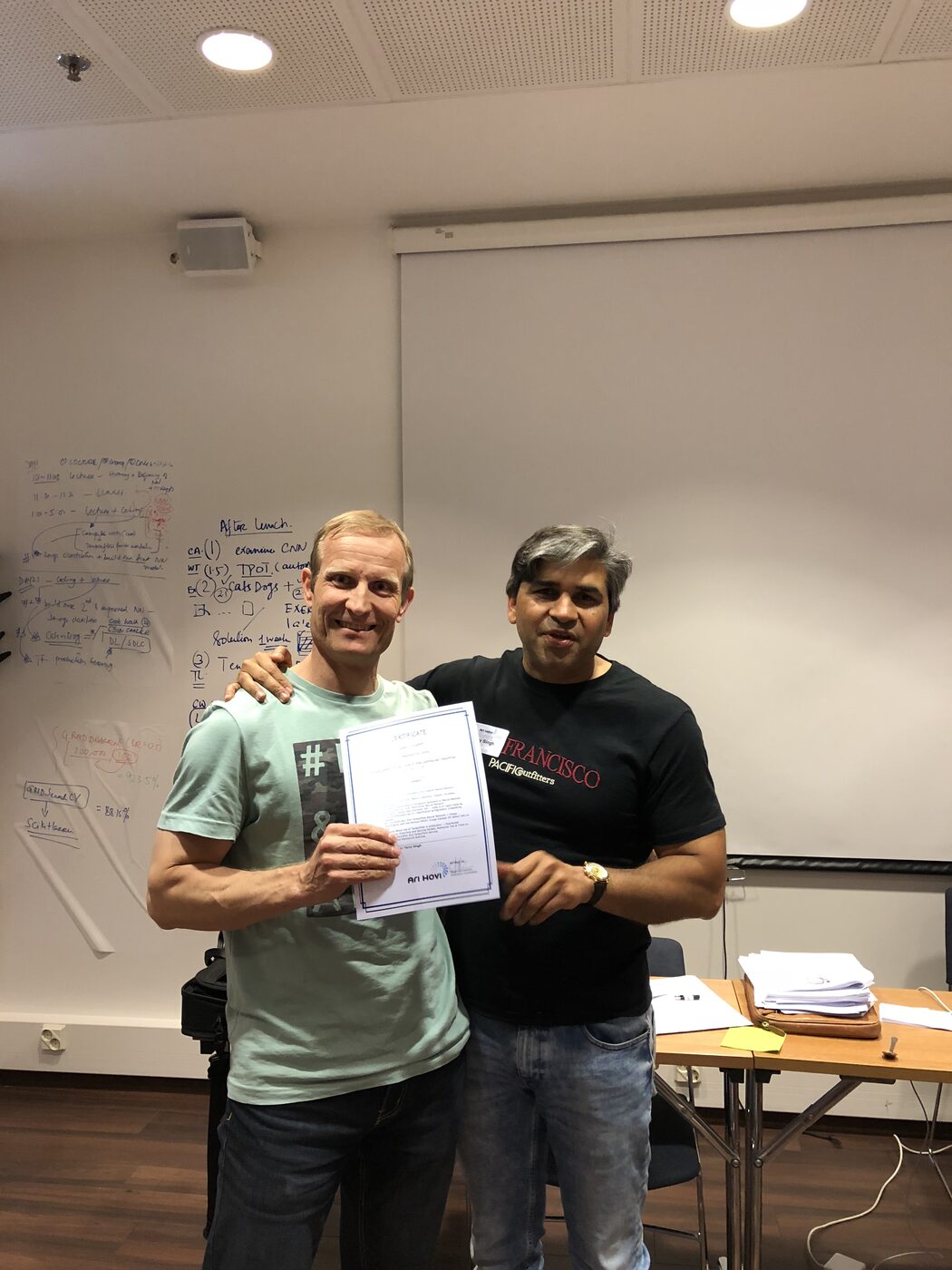 A participant receives his certificate, the two-day agenda still written up on the whiteboard behind.