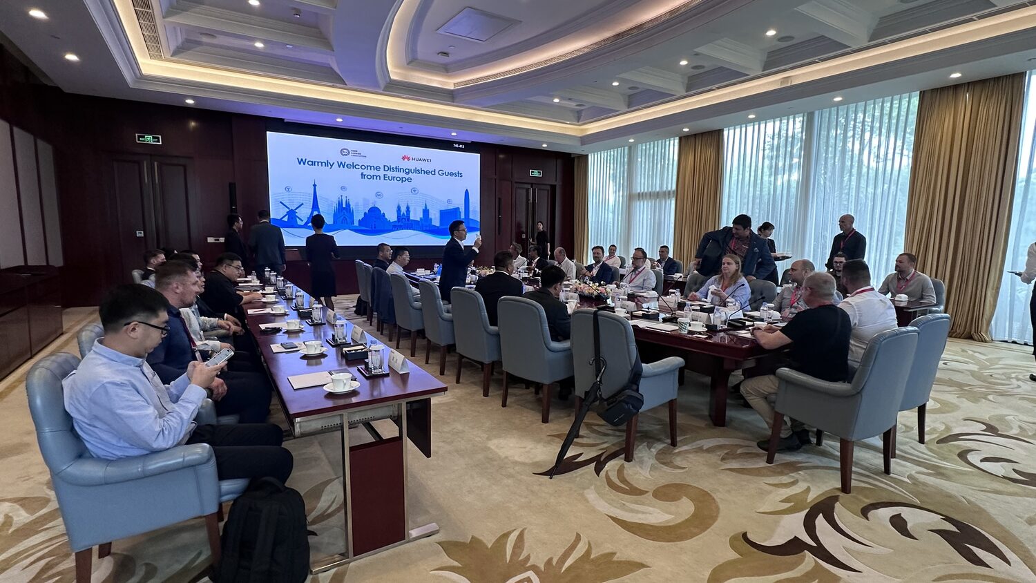 A second meeting room used on 30 June, grey chairs and a long table, delegation seated toward the screen.