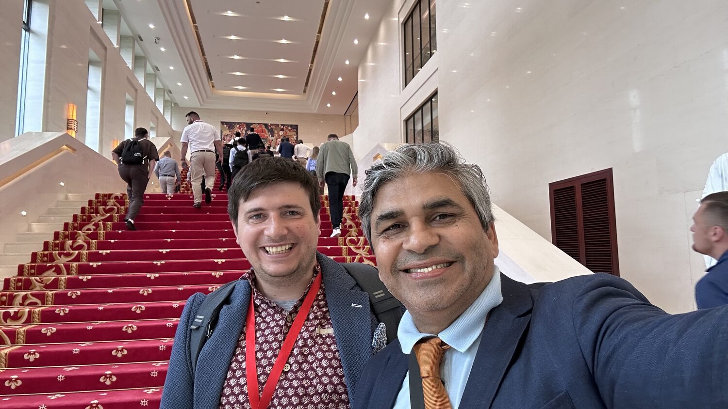 Two delegates in suits and lanyards on the red-carpeted staircase of the Shenzhen venue, 30 June early afternoon.