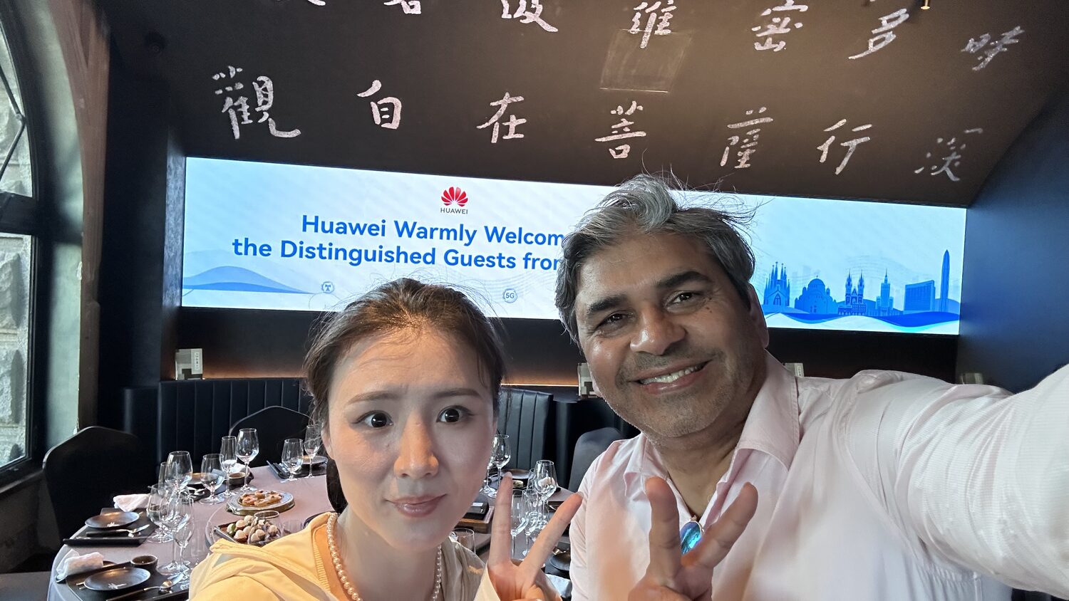 Tarry Singh with a host at the Shanghai dinner venue, the Huawei welcome banner lit on the wall behind, 3 July evening.