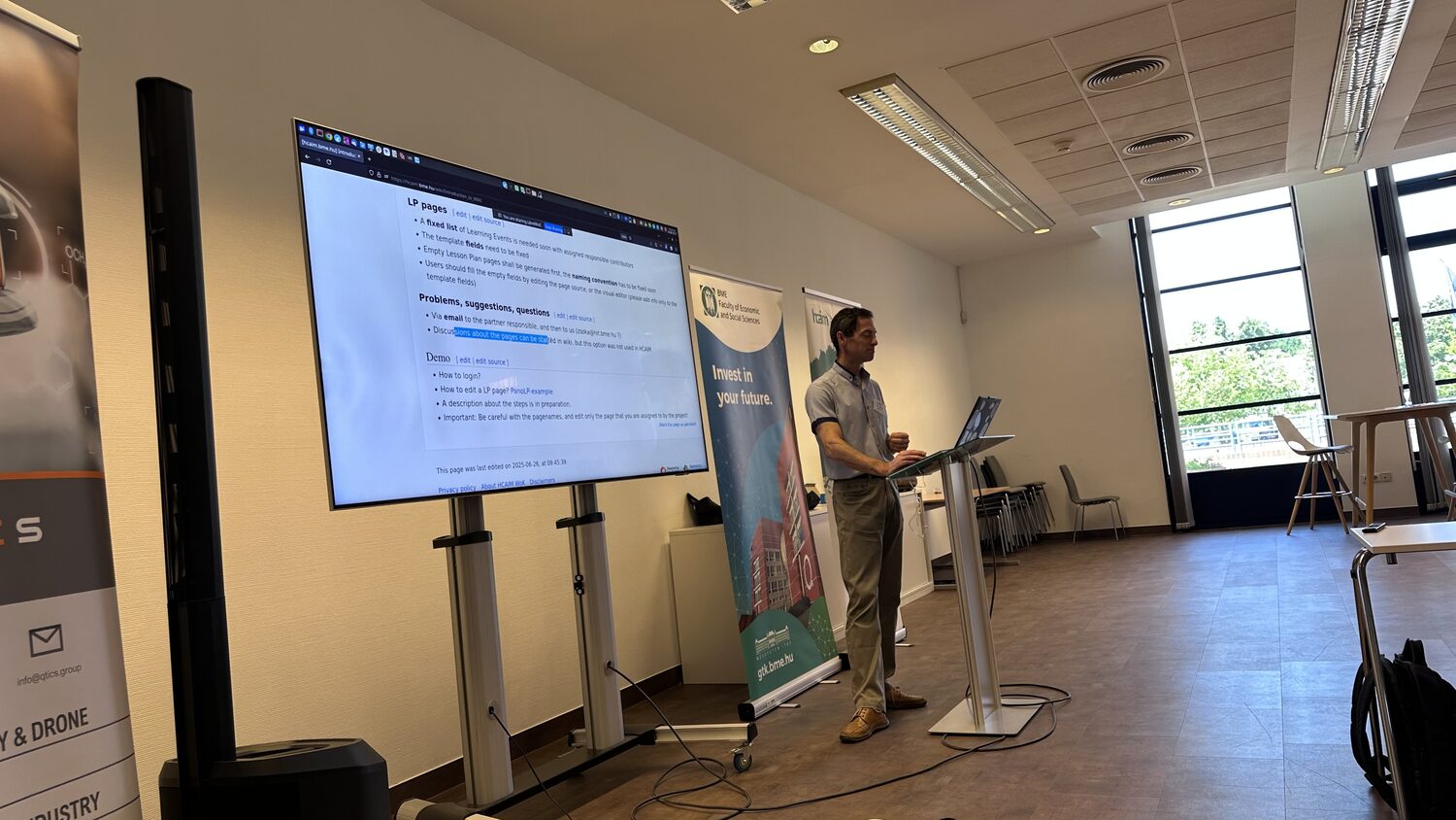 Presenter running the WP3 wiki tutorial from the lectern, the learning-path page projected on the screen.