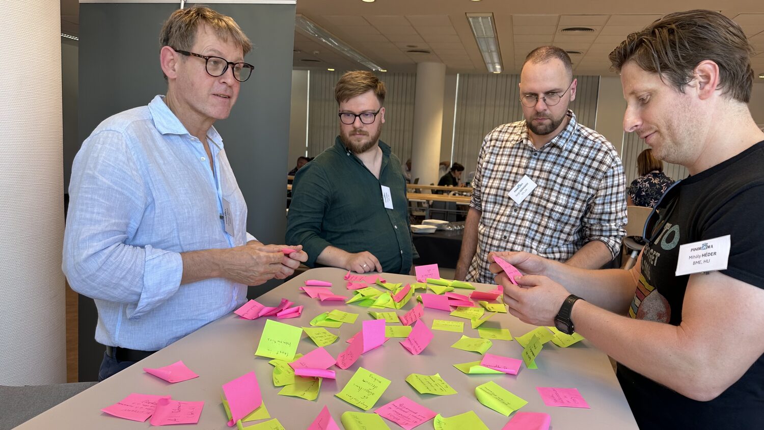 Four partners working over a table of sticky notes, one badge reading Mihály Héder, BME, HU.