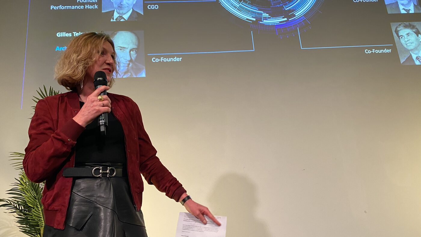 The same speaker, framed wider, with the projected org chart legible behind her and Gilles Teisseyre of Arcturus Group listed as a co-founder for public affairs.