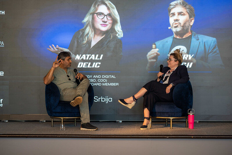 Wide view of the fireside chat, both speakers seated on stage beneath the session graphic.