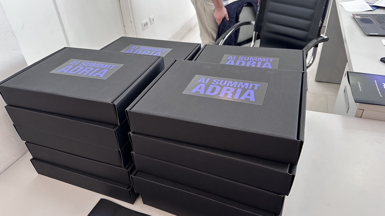 Delegate boxes stacked on a chair, each printed with the AI Summit Adria mark.