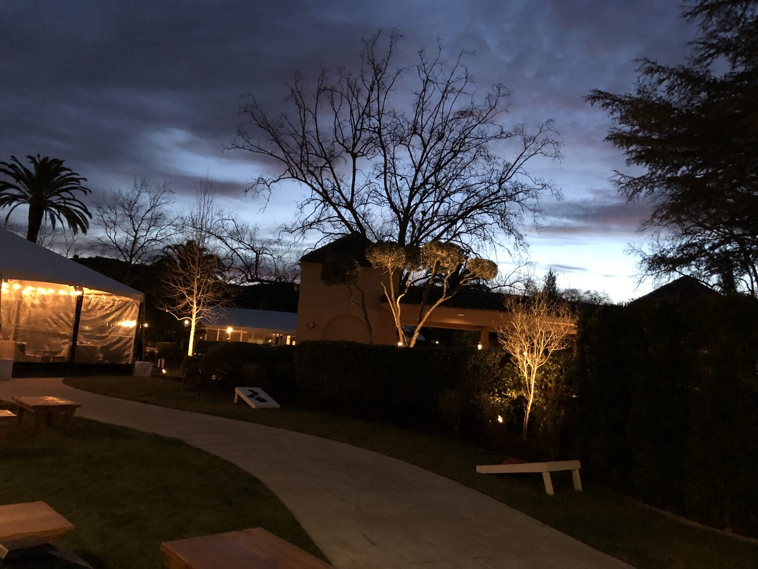 The summit lawn at dusk, the event tent lit from within, benches and lawn games set out on the grass