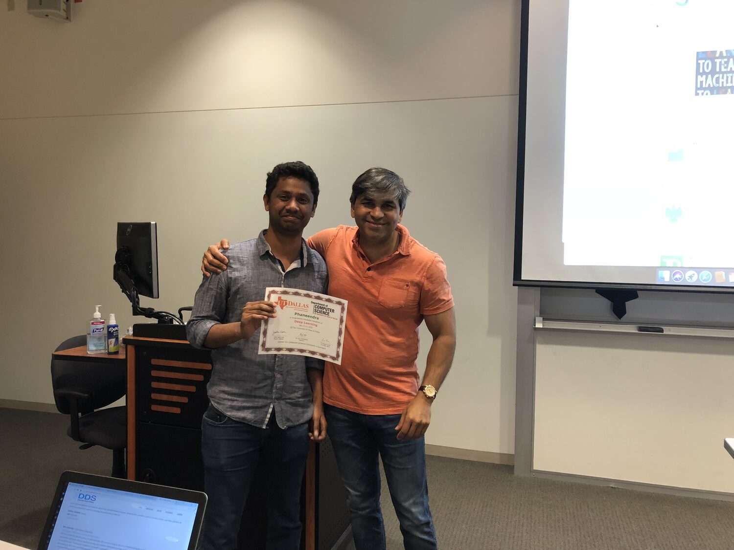 Certificate handover at the podium, screen still lit behind