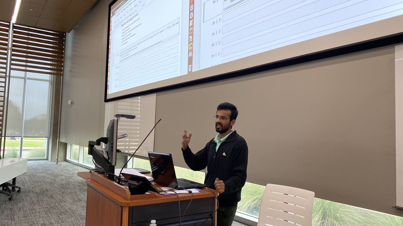 An instructor at the lectern working through code projected across the full width of the hall's screen.