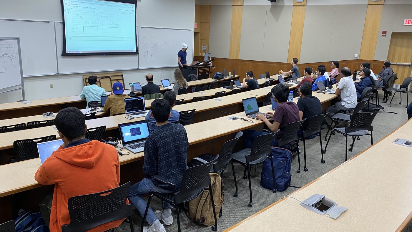 The lecture hall during a session, participants at the benches with laptops open.